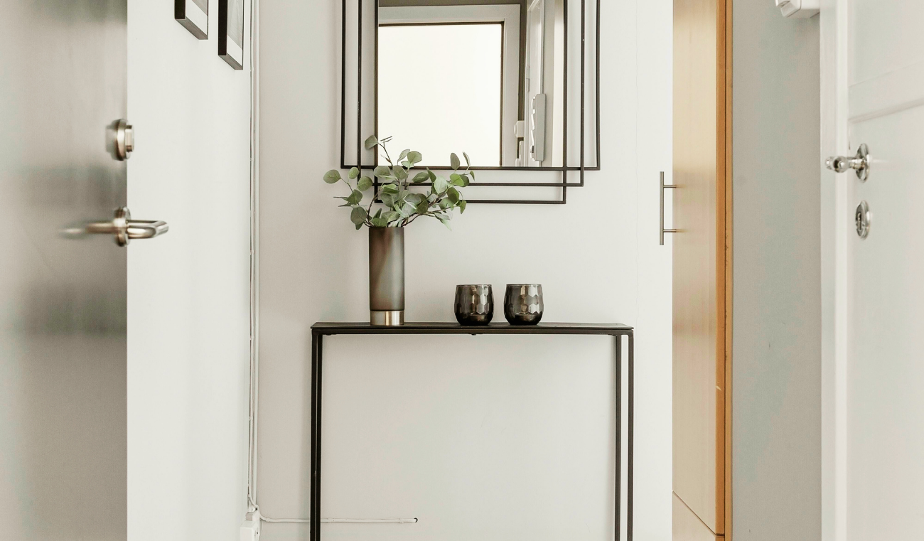 L&rsquo;ingresso &egrave; uno degli spazi pi&ugrave; importanti della casa, anche se spesso viene trascurato. &Egrave; il primo ambiente che accoglie chi entra e, allo stesso tempo, il punto di passaggio che collega l&rsquo;esterno con la zona giorno. Proprio per questo dovrebbe essere funzionale, ordinato e coerente con lo stile dell&rsquo;abitazione. Tuttavia, non sempre si dispone di metrature generose: in molti casi si tratta di spazi stretti, corridoi o piccoli angoli da valorizzare con soluzioni intelligenti. Progettare un ingresso moderno significa trovare il giusto equilibrio tra estetica e praticit&agrave;. Anche pochi elementi ben scelti possono fare la differenza e trasformare completamente la percezione dell&rsquo;ambiente. Uno degli arredi pi&ugrave; utilizzati &egrave; la consolle salvaspazio, ideale per appoggiare chiavi, posta o piccoli oggetti quotidiani. Le versioni pi&ugrave; moderne sono leggere, sospese o dal design minimale, perfette per non appesantire visivamente lo spazio. In alternativa, si possono scegliere mensole sottili che svolgono la stessa funzione ma occupano ancora meno spazio. Un altro elemento fondamentale &egrave; lo specchio, che non solo ha una funzione pratica, ma contribuisce anche ad ampliare visivamente l&rsquo;ambiente. Uno specchio grande o dalla forma particolare pu&ograve; diventare il vero punto focale dell&rsquo;ingresso, riflettendo la luce e rendendo lo spazio pi&ugrave; arioso e luminoso. L&rsquo;illuminazione gioca un ruolo essenziale nella progettazione di un ingresso accogliente. Spesso si tratta di ambienti privi di luce naturale, quindi &egrave; importante studiare punti luce ben distribuiti. Applique moderne, lampade a sospensione o strisce LED integrate possono creare un&rsquo;atmosfera calda e contemporanea, valorizzando al tempo stesso gli arredi. Per mantenere l&rsquo;ordine &egrave; utile inserire contenitori e soluzioni contenitive intelligenti, come mobili con vani chiusi, panche con spazio interno o appendiabiti da parete. Questi elementi permettono di organizzare scarpe, giacche e accessori senza creare disordine visivo, mantenendo l&rsquo;ingresso sempre in ordine. Infine, anche la scelta dei materiali e dei colori contribuisce a definire lo stile dell&rsquo;ambiente. Toni neutri, superfici leggere e materiali naturali aiutano a creare un ingresso armonioso e moderno, mentre piccoli dettagli decorativi possono aggiungere personalit&agrave; senza appesantire lo spazio. Arredare bene l&rsquo;ingresso significa quindi sfruttare ogni centimetro con soluzioni pratiche ma curate nel design. Un ambiente ben progettato non solo migliora la funzionalit&agrave; della casa, ma trasmette subito una sensazione di ordine e accoglienza fin dal primo passo.